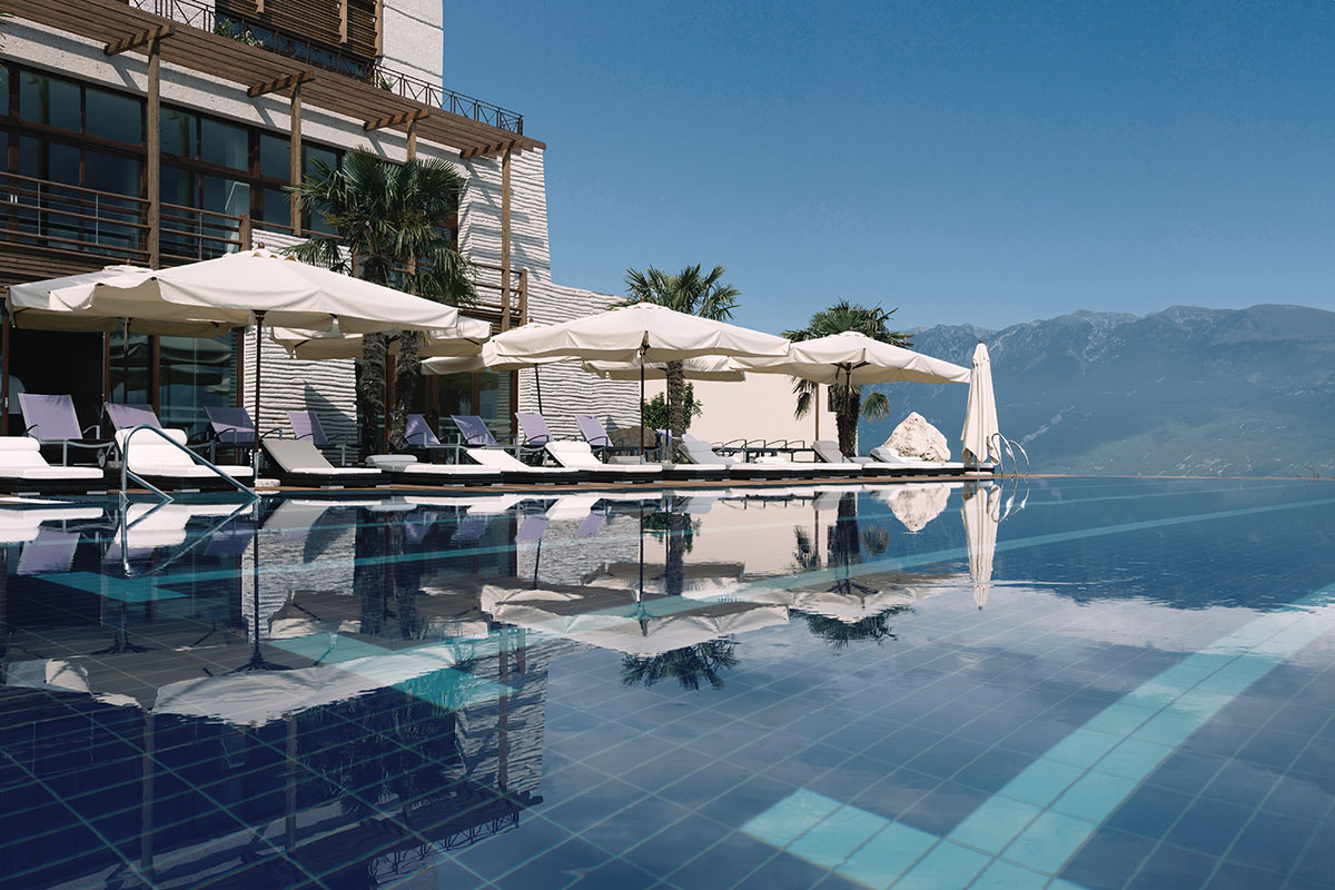 View from the outdoor pool of Lefay Lago di Garda looking into the terrace with shades and the mountains on the other side of Lake Garda in the background