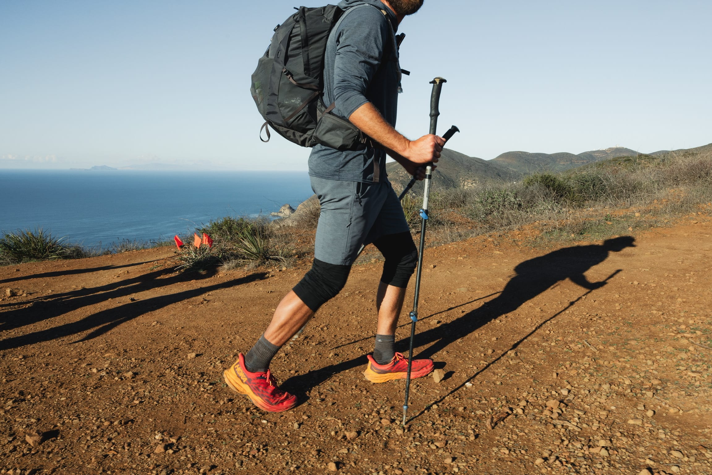 Male guest in hiking gear on a trail with background view over the Pacific Ocean