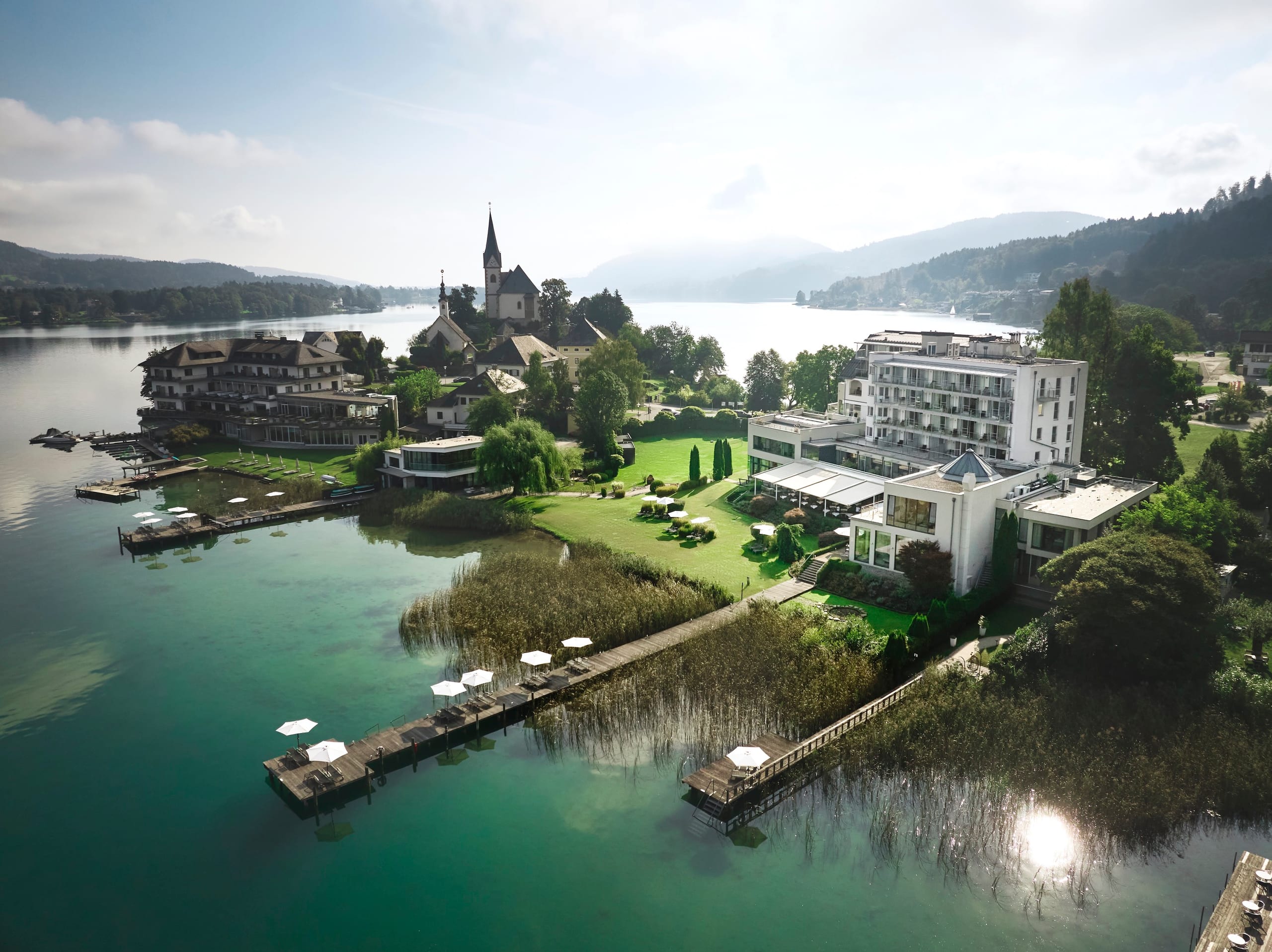 Drone photo above the lake with VIVAMAYR clinic in the middle ground and Maria Woerth and mountains in the background