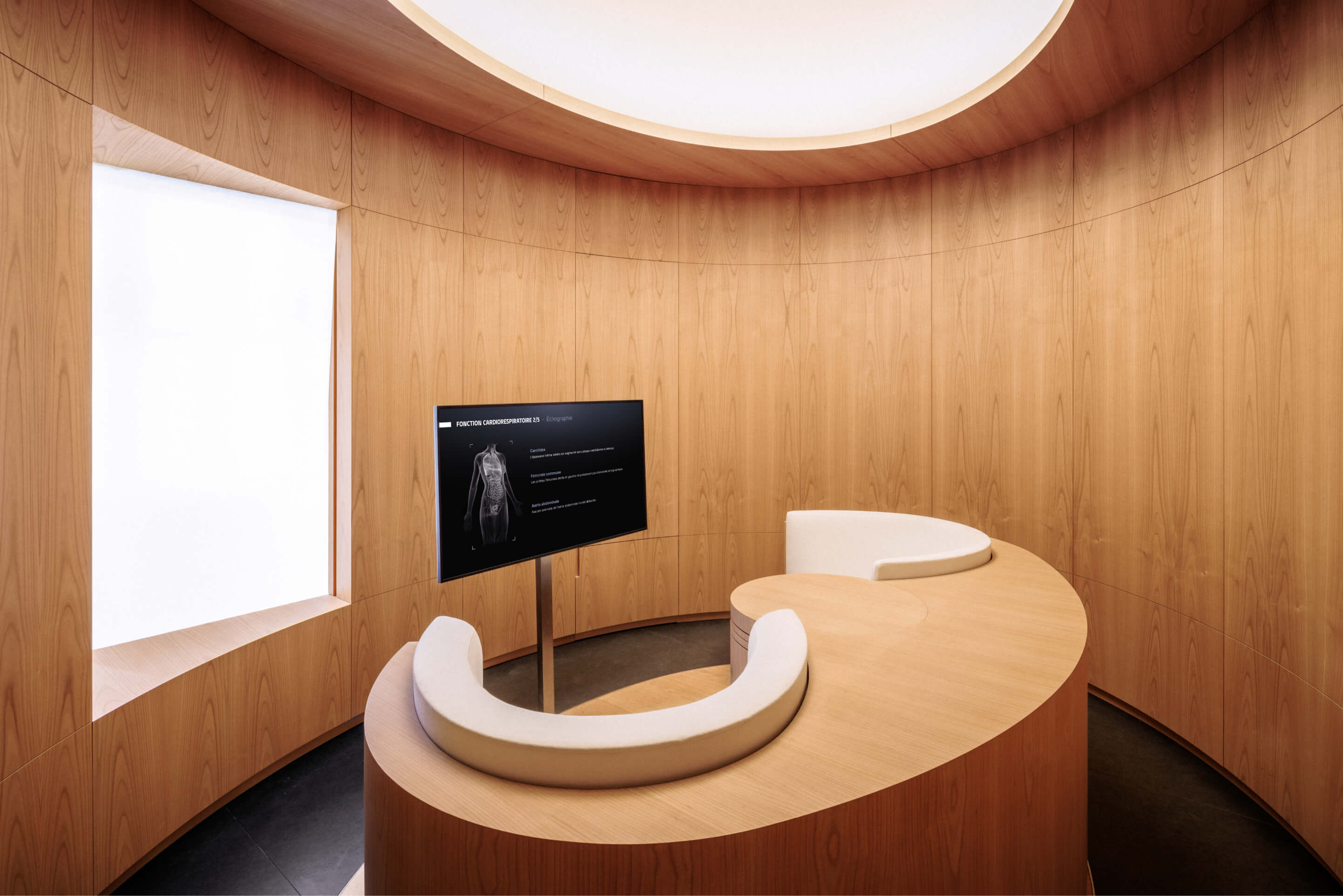 A wooden consultation room with a TV screen showing medical results and beautiful designer seats