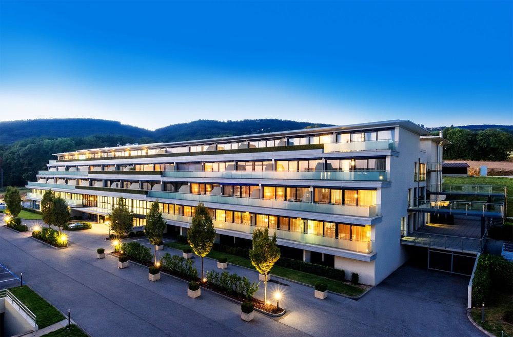Clinique Nescens building illuminated at twilight against the Swiss Jura mountains in Genolier